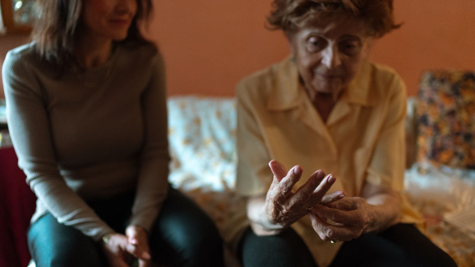 Une femme âgée gesticule en parlant, assise sur un canapé à côté d'une femme plus jeune