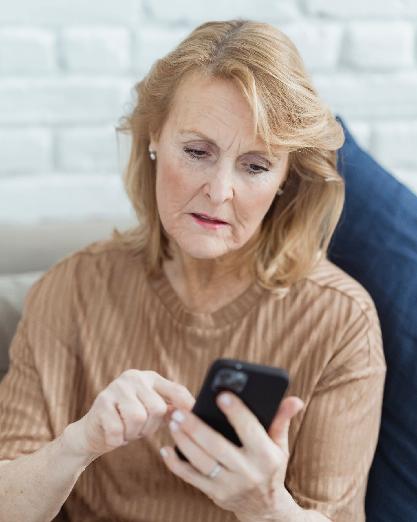 Une femme âgée regarde un téléphone, assise sur un canapé