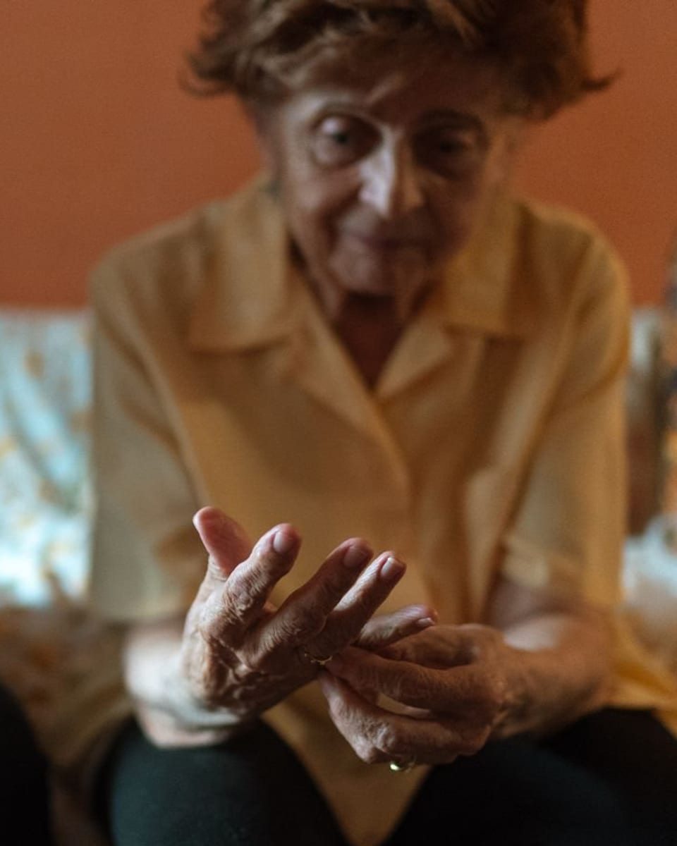 Une femme âgée pensive, assise sur son canapé, les mains jointes